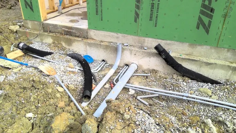 Gray electrical conduits and black flexible piping emerge from the foundation of a new building site