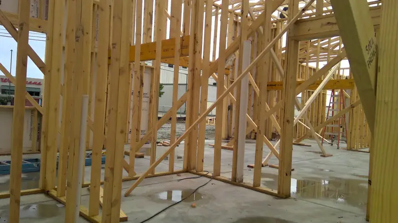 Interior view of wooden wall frames and PVC piping on a concrete slab at a construction site