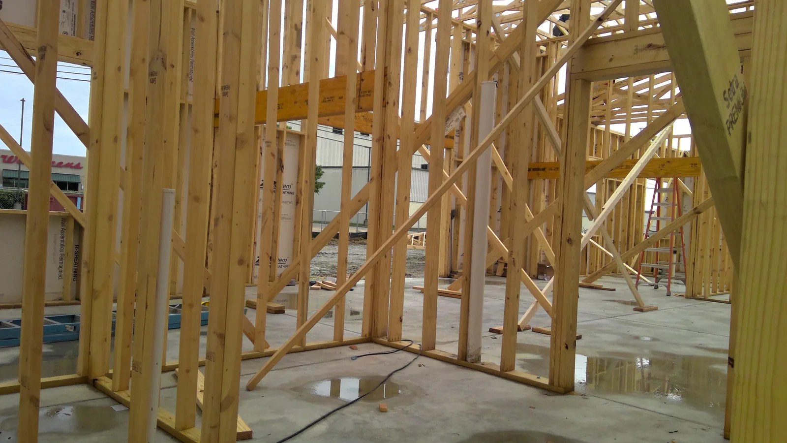 Interior view of wooden wall frames and PVC piping on a concrete slab at a construction site