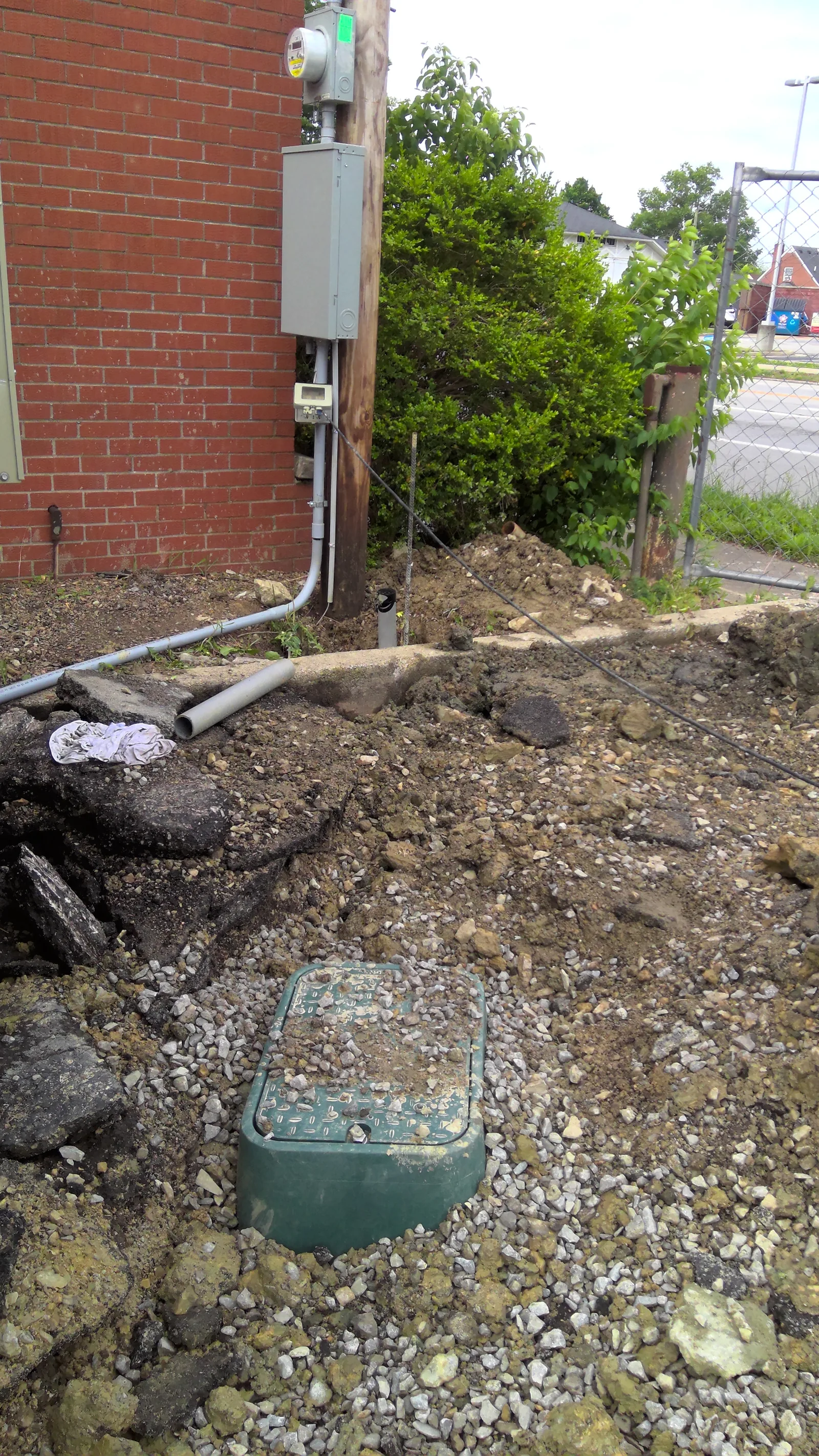 An outdoor electrical meter and grey utility boxes mounted on a wooden pole by a brick wall