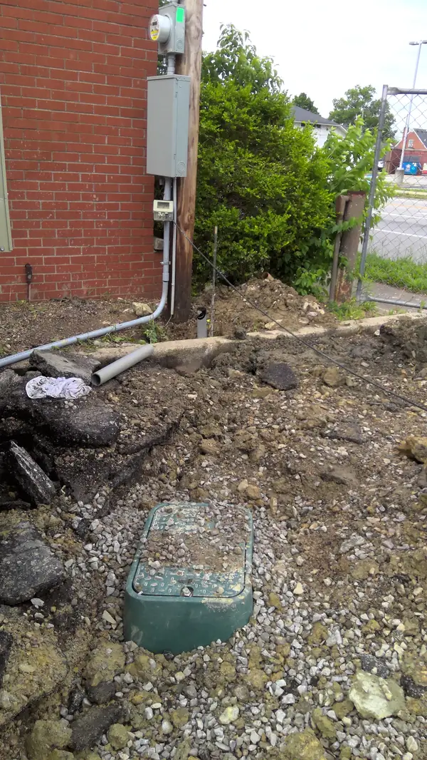 An outdoor electrical meter and grey utility boxes mounted on a wooden pole by a brick wall