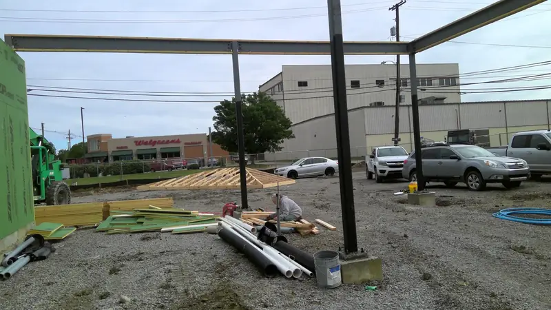 A construction site with steel beams, underground pipes, lumber, and workers at a new bank branch