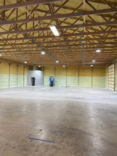 Open warehouse interior with exposed wood trusses and a bare concrete floor, being converted into an indoor soccer training facility