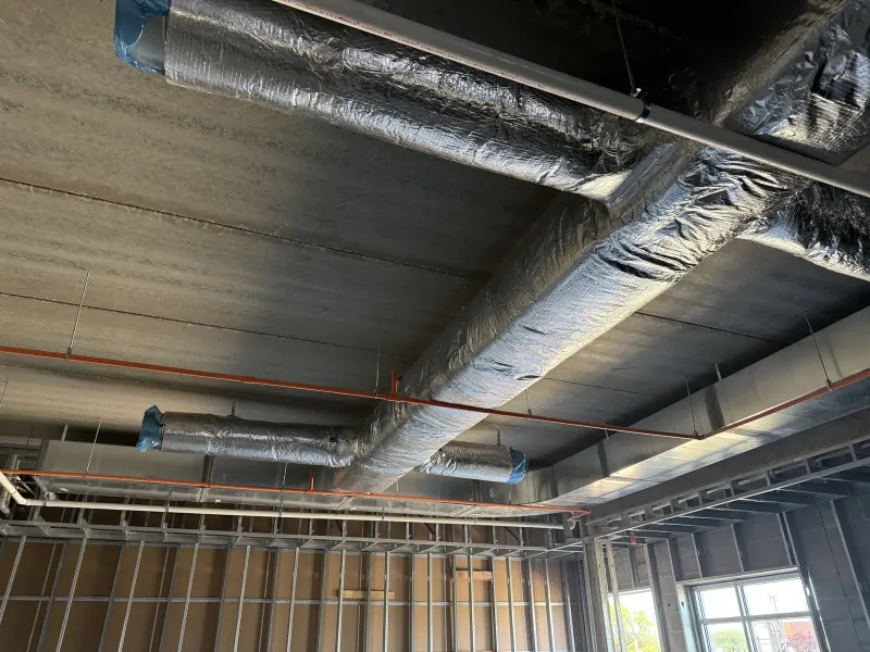 Insulated silver ductwork and metal wall framing under a concrete ceiling during hotel construction
