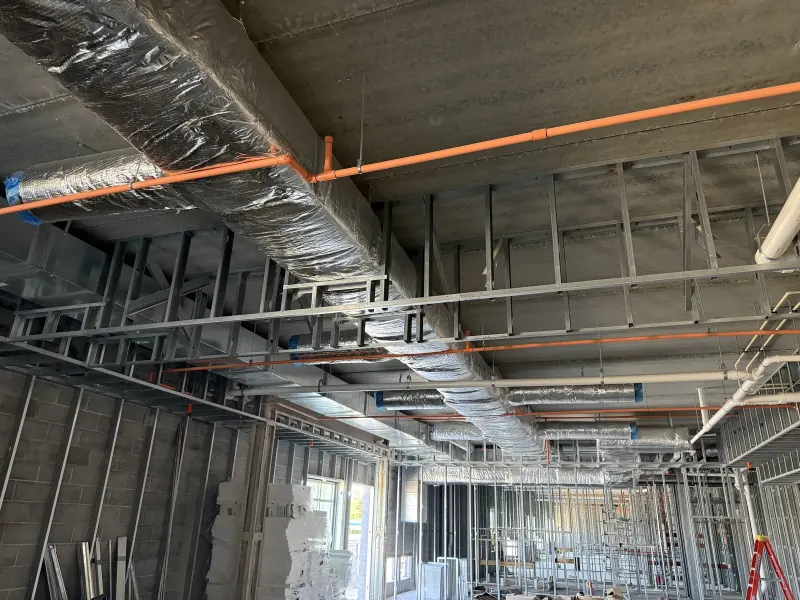 Insulated air ducts and orange fire sprinkler pipes installed above metal wall framing in a hotel building