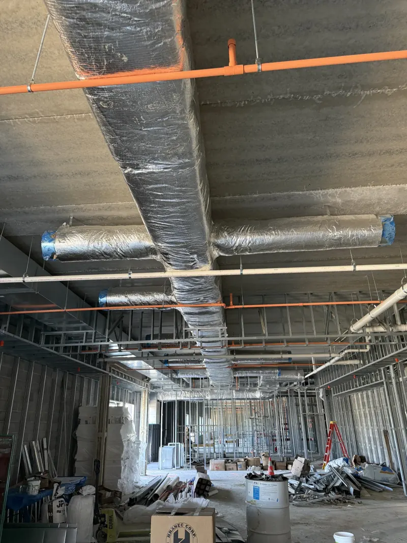 Insulated silver ductwork and orange fire sprinkler pipes installed on a concrete hotel ceiling