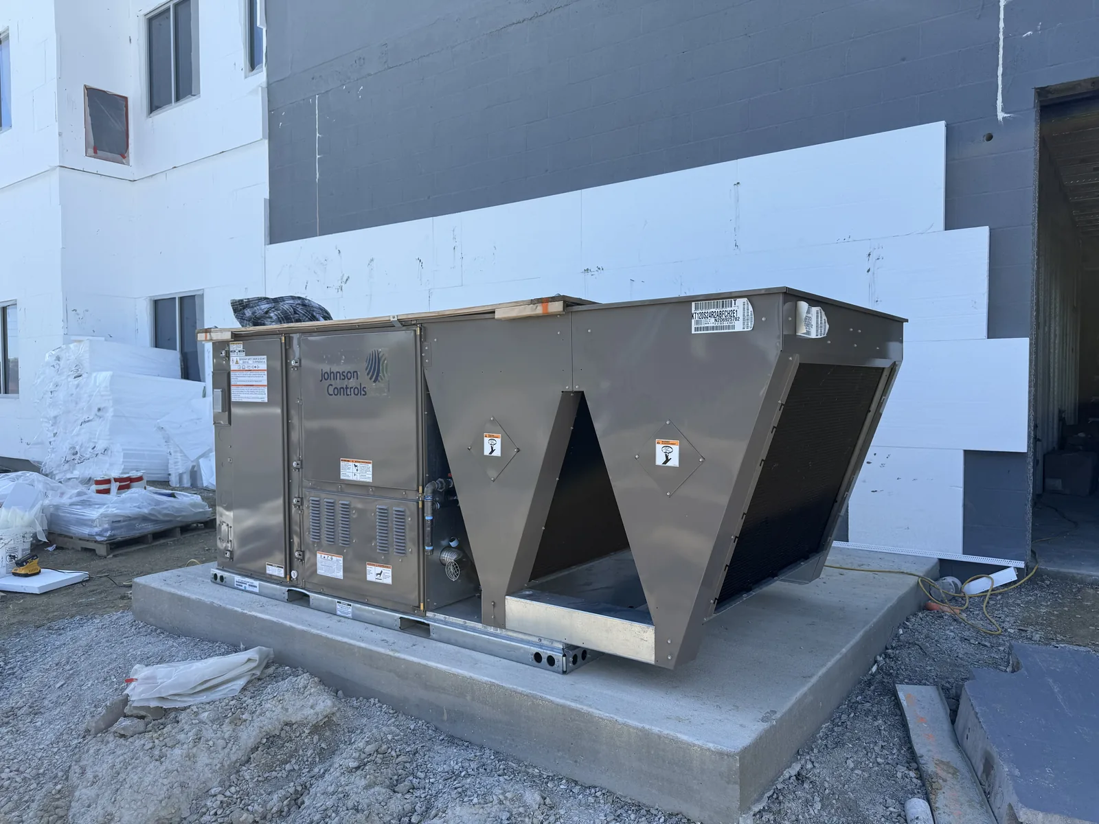 A large grey commercial HVAC unit sits on a concrete pad at a construction site