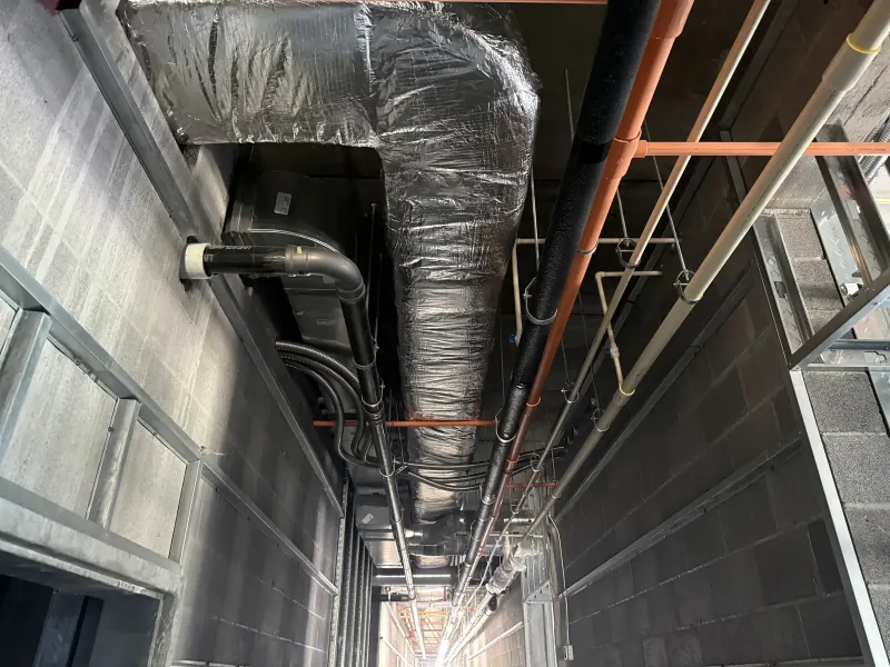 Insulated silver ductwork and various pipes installed above a hotel hallway during new construction