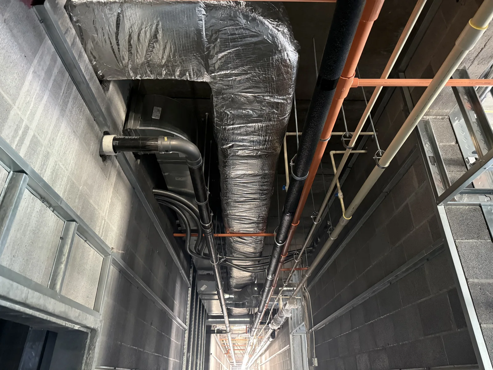 Insulated silver ductwork and various pipes installed above a hotel hallway during new construction