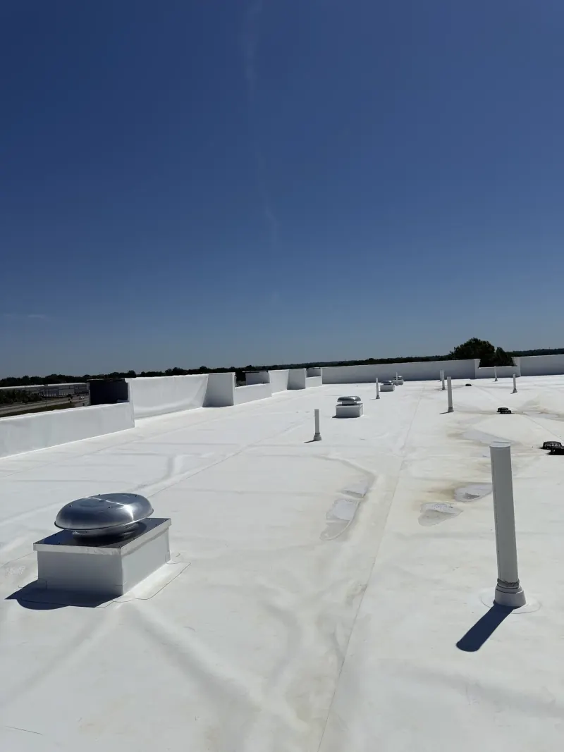 A flat white commercial roof with several metal vent fans and white vertical exhaust pipes