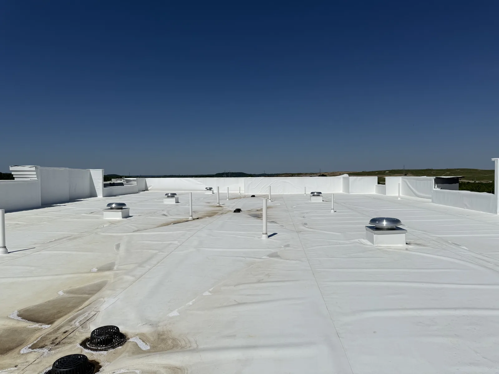A flat white commercial roof with several metal vents and tall white exhaust pipes installed across it