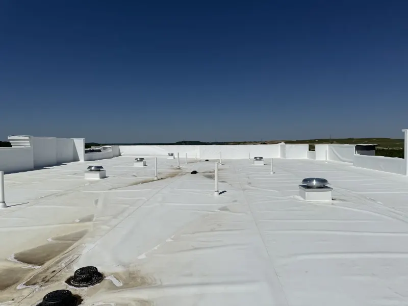A flat white commercial roof with several metal vents and tall white exhaust pipes installed across it