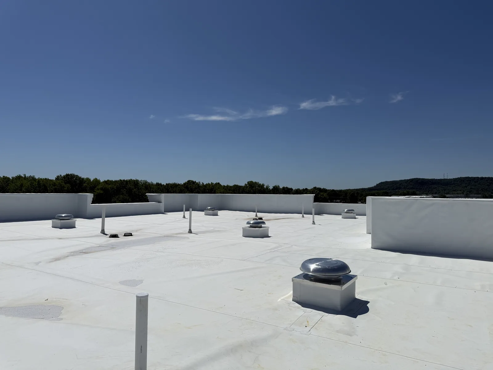 Several silver metal exhaust fans and white PVC pipes on top of a flat white hotel roof