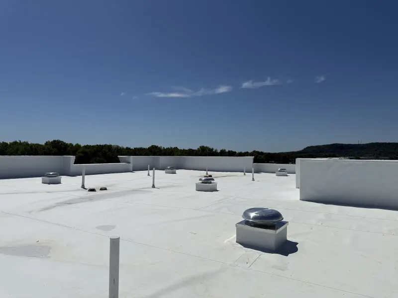 Several silver metal exhaust fans and white PVC pipes on top of a flat white hotel roof
