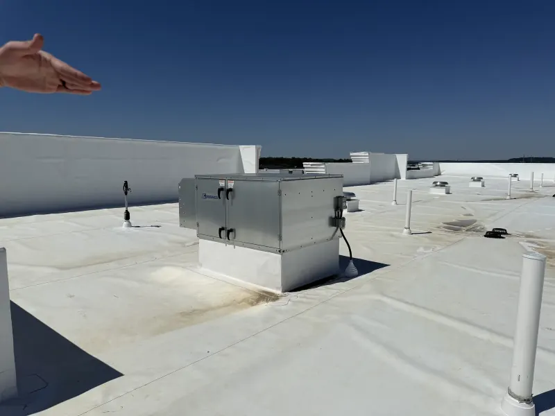 A stainless steel HVAC unit sits on a white commercial rooftop under a clear blue sky