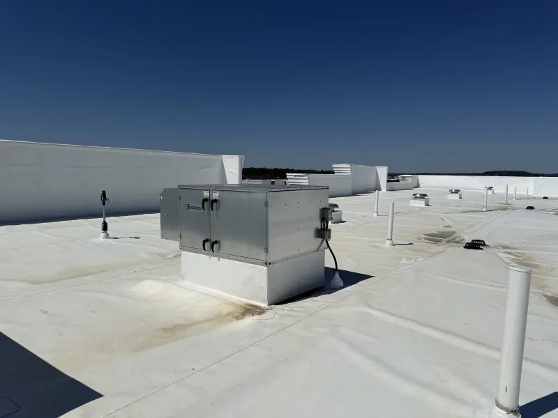 A large silver metal HVAC unit on a white flat roof with several white vent pipes
