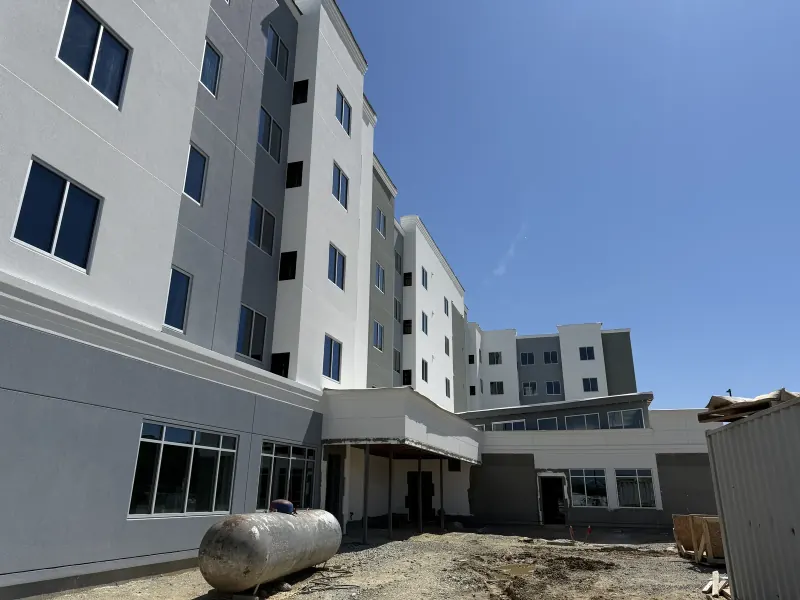 A modern multi-story hotel exterior under construction with white and gray siding and many large windows