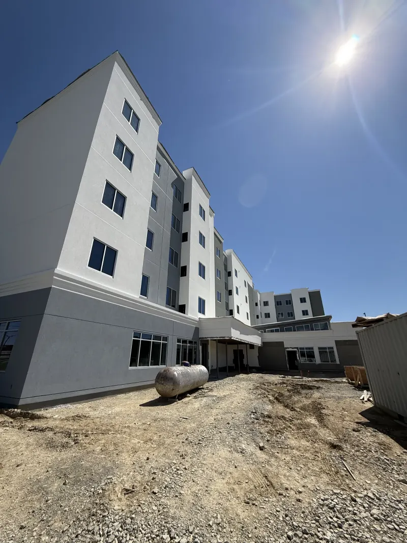 A multi-story hotel building under construction with a large gray gas tank sitting on dirt
