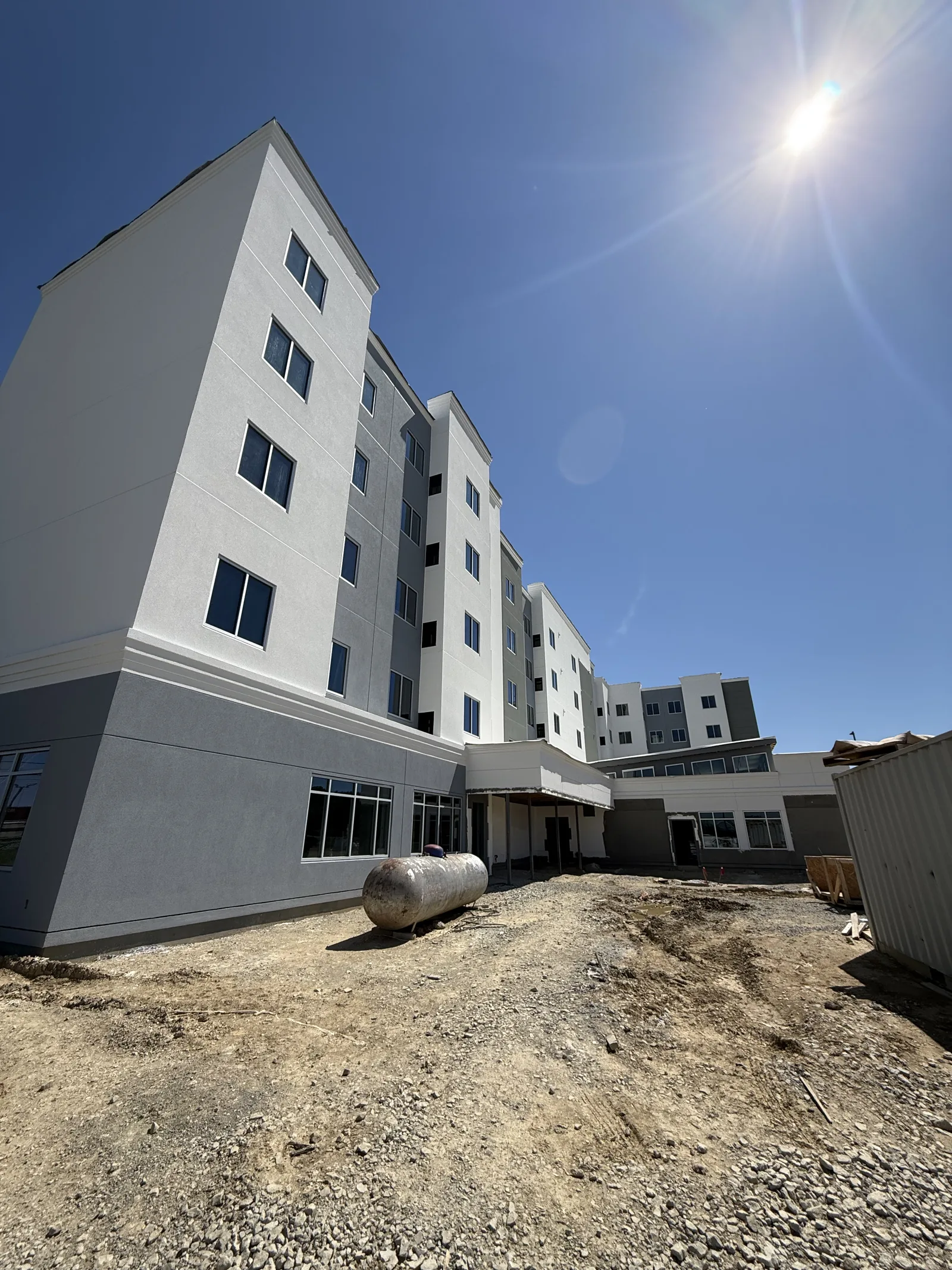 A multi-story hotel building under construction with a large gray gas tank sitting on dirt