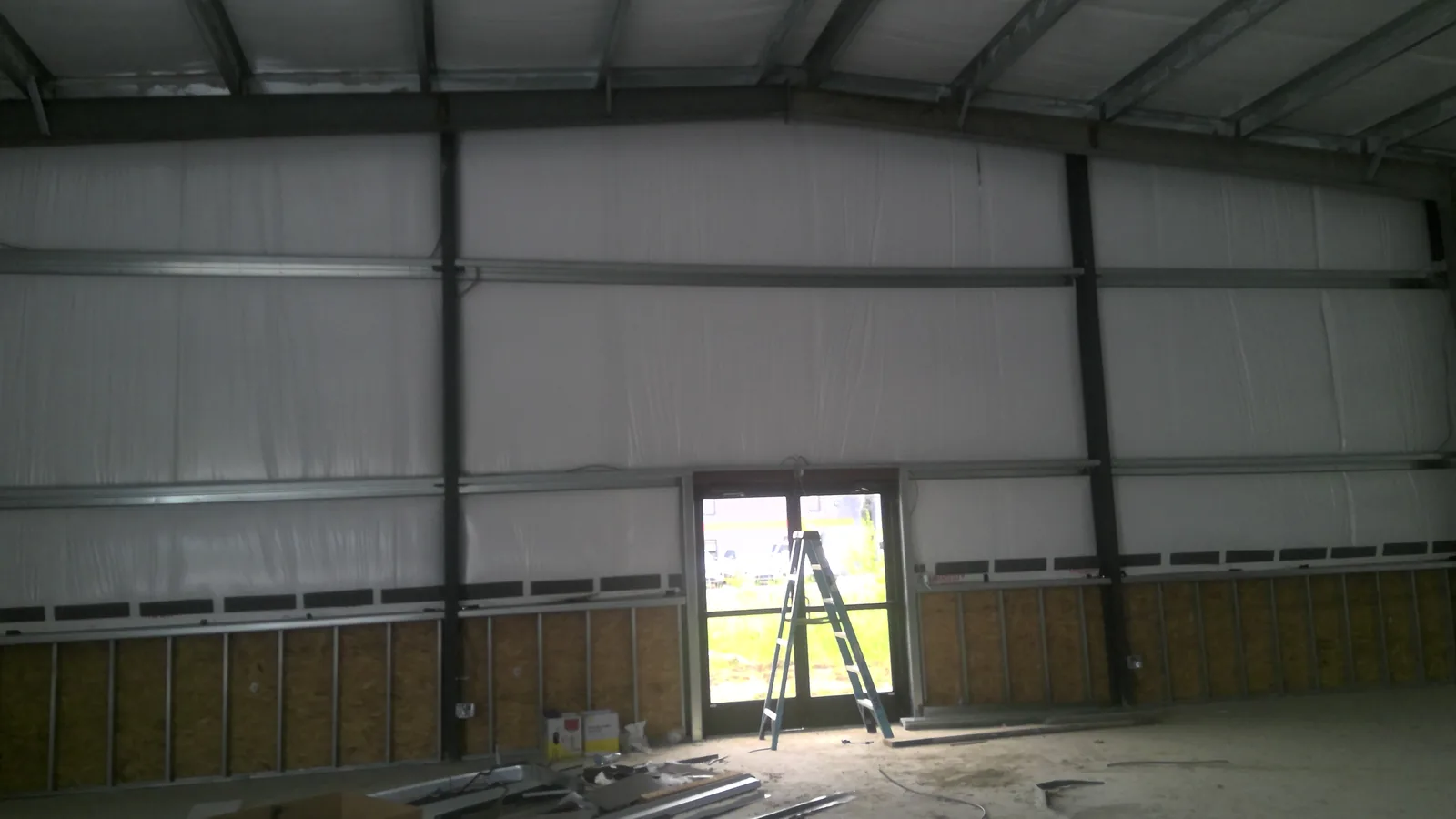 Interior warehouse wall under construction with white insulation, steel beams, and a step ladder near a door