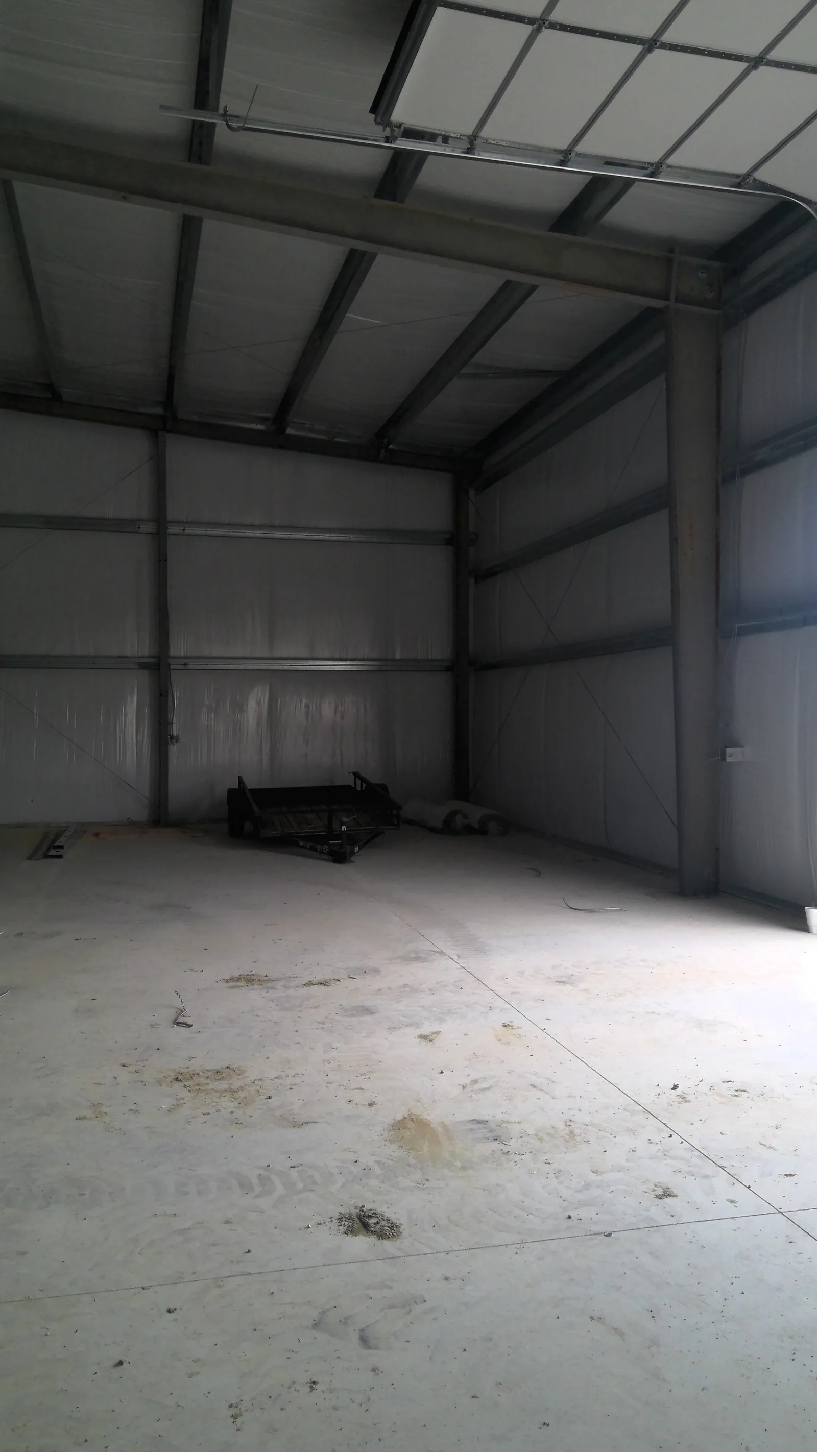 Interior view of an empty warehouse with metal wall panels, concrete floors, and a garage door
