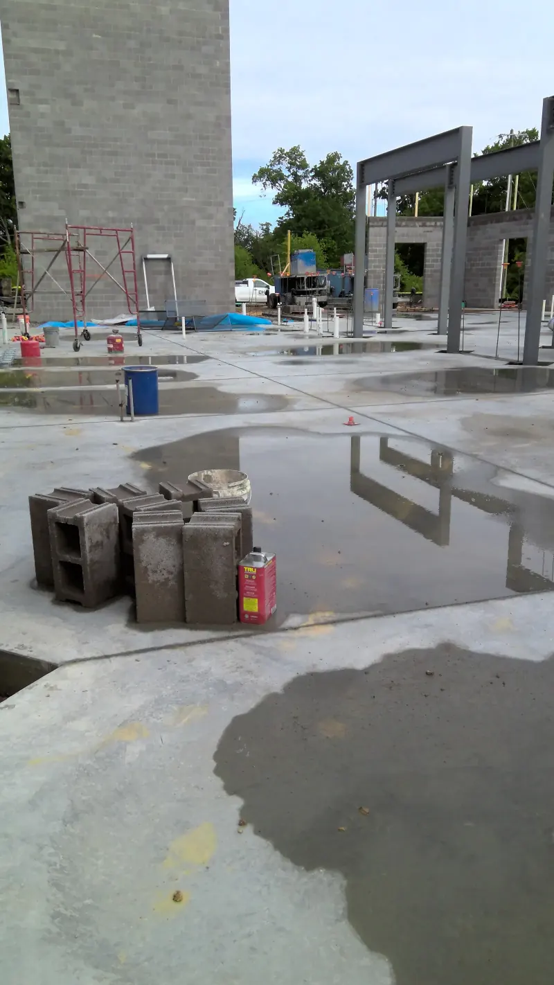 Concrete floor slab with building materials and steel frame at a hotel construction site with water puddles