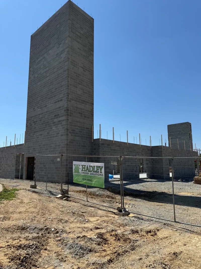 A masonry construction site with a Hadley Energy Solutions sign on a metal fence