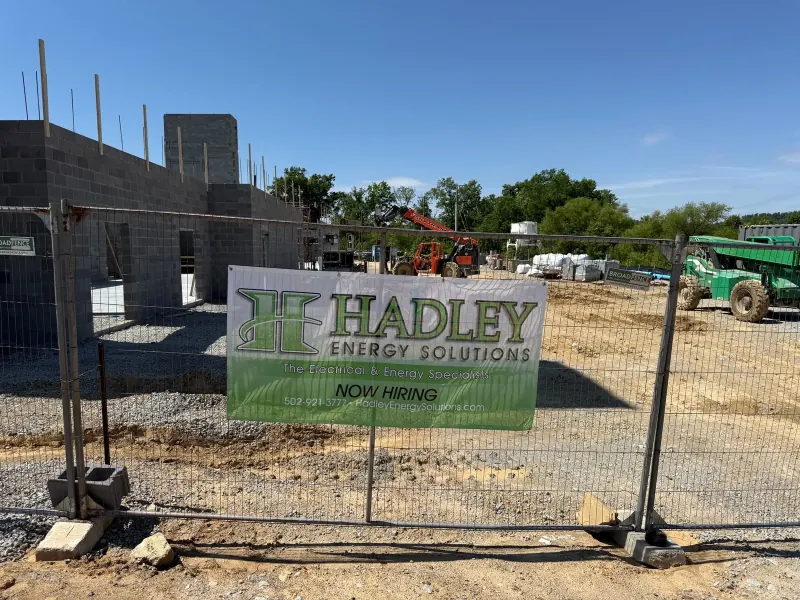 A construction site fence with a large company sign in front of a concrete block building