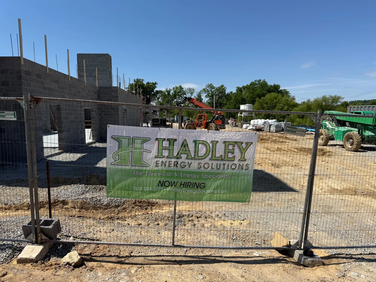 A construction site fence with a large company sign in front of a concrete block building